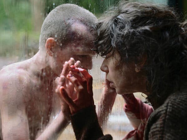 A child with a buzz cut puts their hands to glass. A woman stands on the other side, holding out her hands.